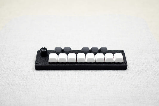 The ParksTool 13KS-1ES at an angle on a linen surface: eight white keys along the front, five black keys behind them, and an encoder knob at the left end